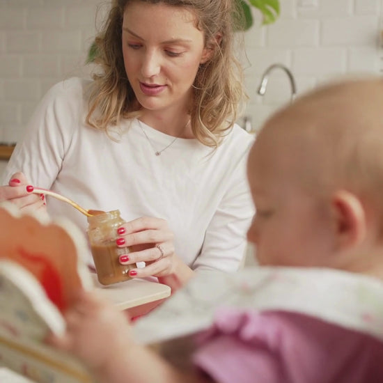 A mother feeding her baby mashed potatoes in the kitchen.