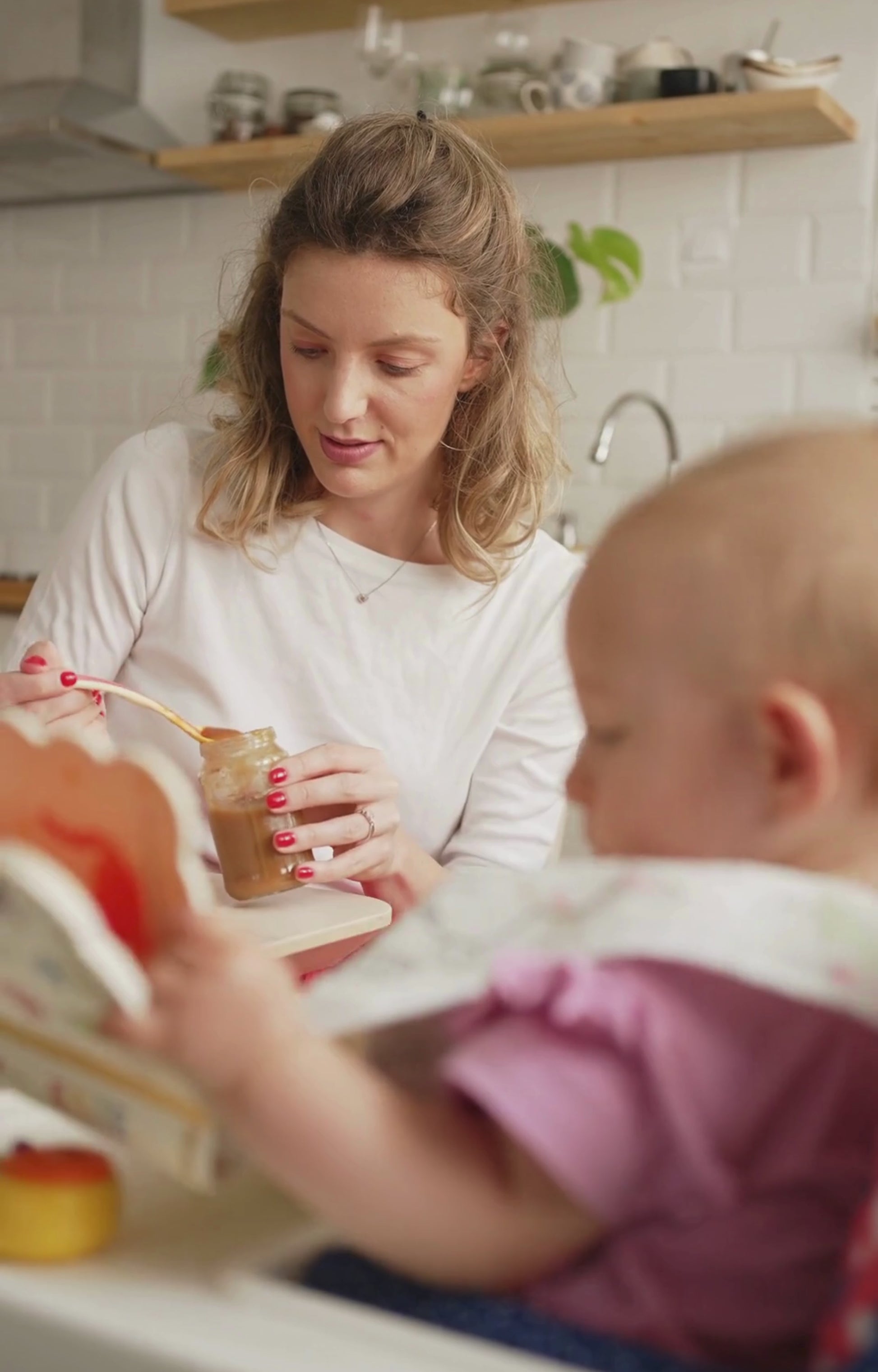 A mother feeding her baby mashed potatoes in the kitchen.